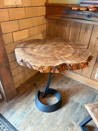 Wooden table with a natural edge and metal base in a rustic setting.